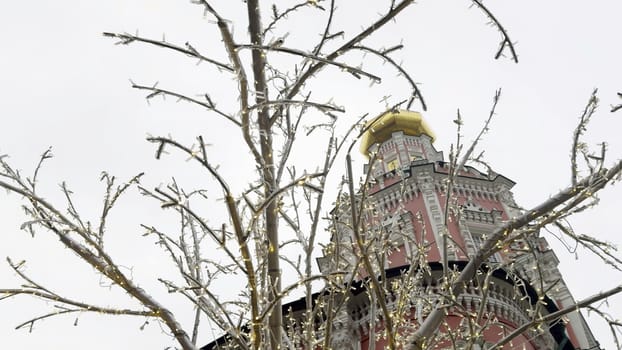 Christmas lights decorating bare tree branches in front of novodevichy convent bell tower in moscow, russia