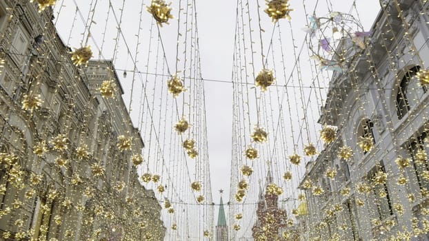 Festive atmosphere in moscow with golden decorations illuminating nikolskaya street, featuring the kremlin tower in the distance