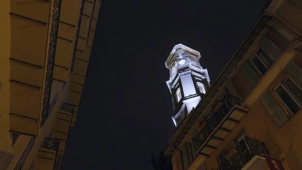 White bell tower standing tall against dark night sky, viewed from narrow street