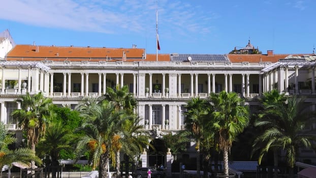 Majestic prefecture building with waving french flag, palm trees, and blue sky in nice, france