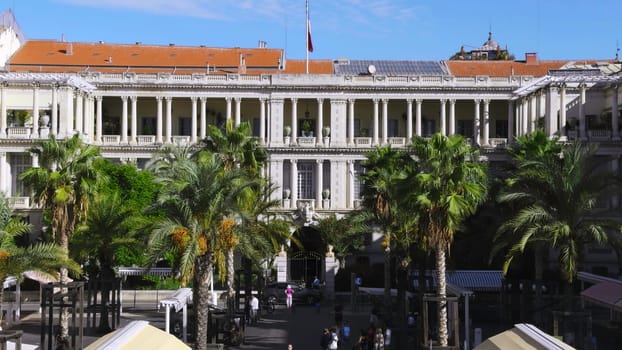 Majestic prefecture building with waving french flag, palm trees, and blue sky in nice, france