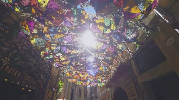 Umbrellas and decorations suspended above a pedestrian street create a vibrant and celebratory ambiance