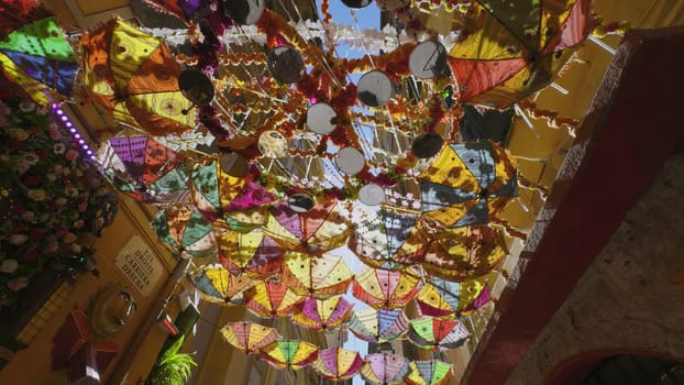 Umbrellas and decorations suspended above a pedestrian street create a vibrant and celebratory ambiance