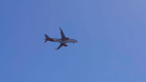 White and red passenger airplane is flying and turning in the clear blue sky