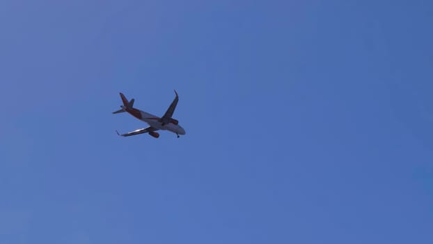 White and red passenger airplane is flying and turning in the clear blue sky
