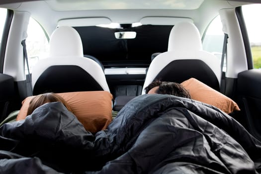 Cozy travel rest in car with two people sleeping in back seat on pillows.