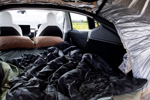 Camping setup inside car with sleeping bags and pillows for outdoor adventure.