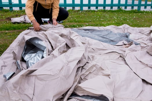 Young male setting up beige tent outdoors on green grass.
