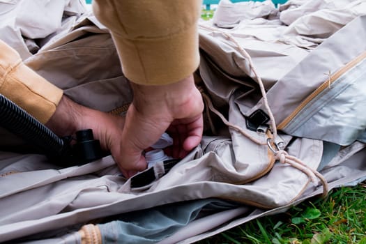 Setting up inflatable tent with manual air pump on grass by caucasian male adult.