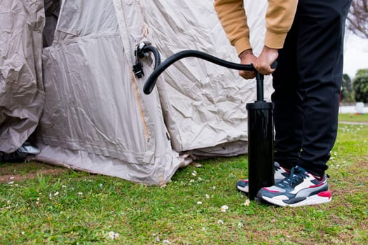 Young hispanic adult male inflating tent outdoors with hand pump.