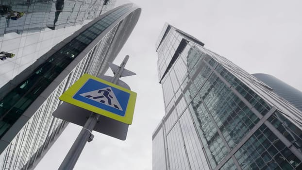 This dramatic view highlights towering skyscrapers next to a pedestrian sign in a busy urban environment. Action