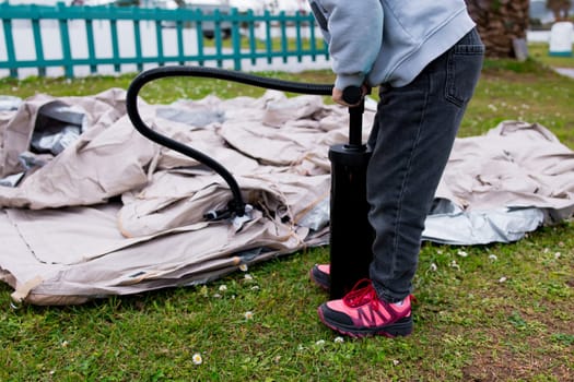 Child inflating tent with pump in outdoor park setting.