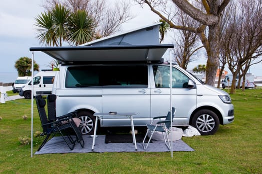 Camper van setup with awning and chairs in scenic campsite.