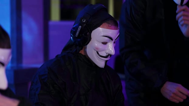 A mysterious masked figure dressed in dark attire captivates the attention of everyone present in a vibrant atmosphere. Media