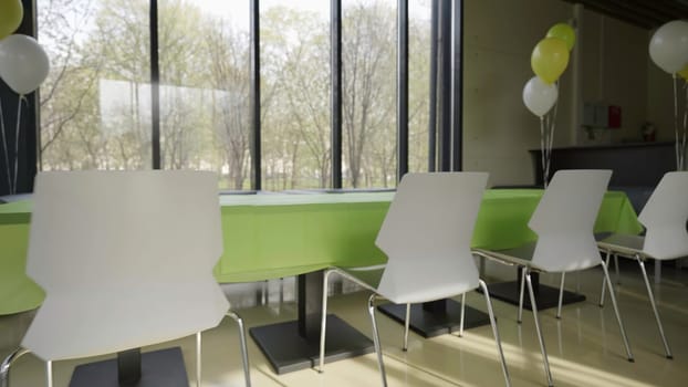The video shows a cheerful dining room decorated festively with a green tablecloth, white chairs, colorful balloons, and ample natural light. Creative
