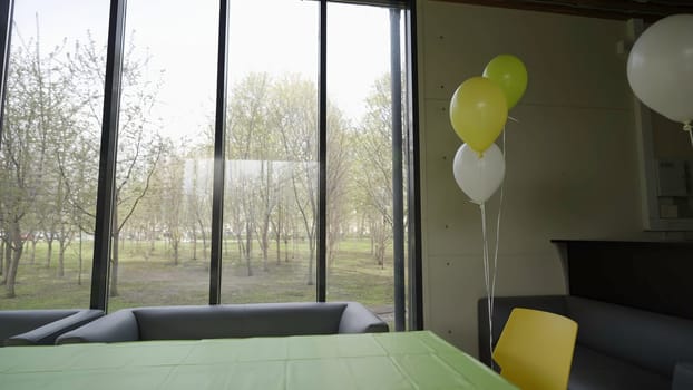 The video shows a cheerful dining room decorated festively with a green tablecloth, white chairs, colorful balloons, and ample natural light. Creative