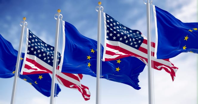 Multiple American and European Union flags flutter outdoors in the wind, symbolizing diplomacy, unity, freedom, and international relations. 3D illustration with selective focus on blue sky background