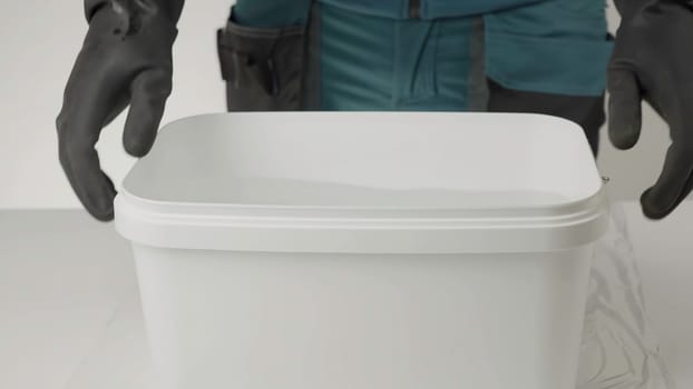 In this video, a person in black gloves demonstrates the opening of a white plastic container, revealing water inside, in a clean workspace. Creative