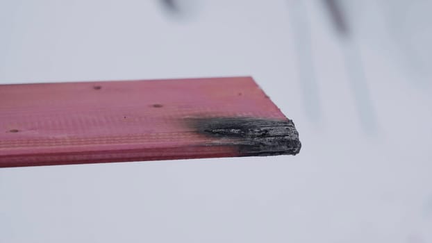 The video shows a closeup of wood affected by fire. A flame bursts, heating the wood, which becomes charred and loses pieces. Smoke rises, indicating transformation and the aftermath of combustion. Creative