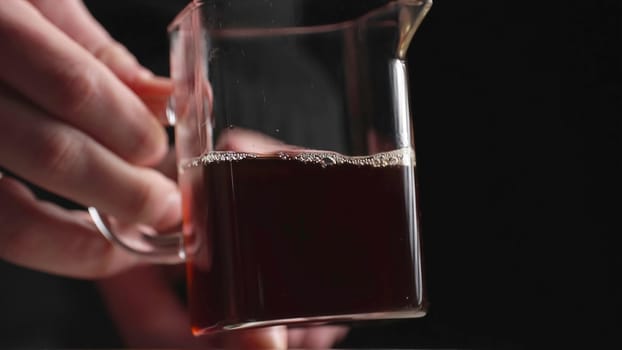 A closeup of a glass pitcher with dark liquid, elegantly displayed against a striking black background. Media