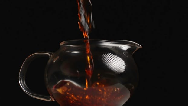 A stunning and beautiful shot of steaming tea being gracefully poured into a glass teapot against a black background. Media