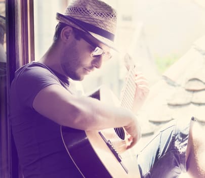 Young man sitting on the window playing the guitar