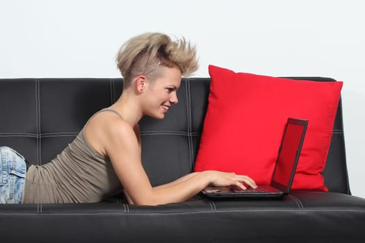 Fashion woman browsing internet in a laptop at home lying on a black couch