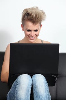 Fashion teenager girl at home sitting on a couch browsing in a laptop