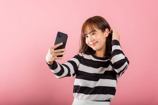 Happy Asian portrait beautiful cute young woman smiling excited making selfie photo, video call on smartphone studio shot isolated on pink background, female hold mobile phone raise hand say hello