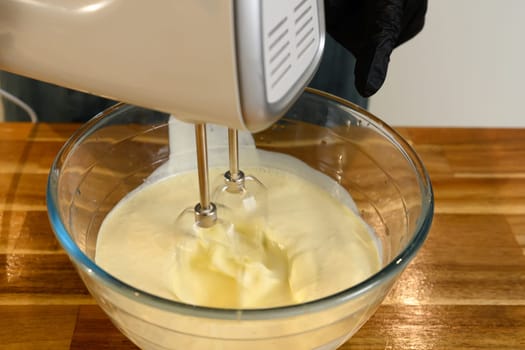Close up of an electric hand mixer blending cream in a glass bowl.