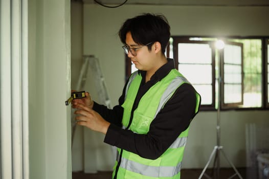 Engineer using a measuring tape to check wall dimensions at construction site.