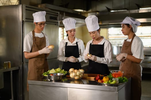 Young chefs collaborating on food preparation during hands on cooking class at culinary school.