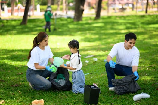 Parents and child volunteering together by collecting trash and cleaning up a park.