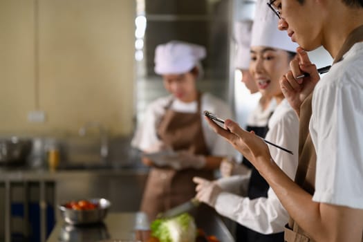 Culinary students collaborating and checking a recipe plan during a cooking class.