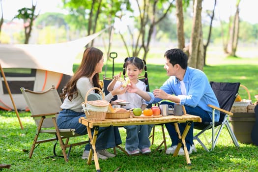 Smiling parents and daughter sharing food in nature while camping in the forest.