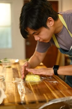 Young asian man shaping freshly made compound butter with herbs on kitchen counter.