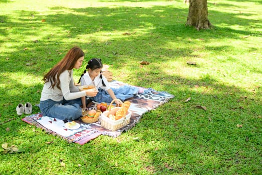 Mother and daughter enjoying picnic on blanket with fresh bread and fruits in a sunny forest.