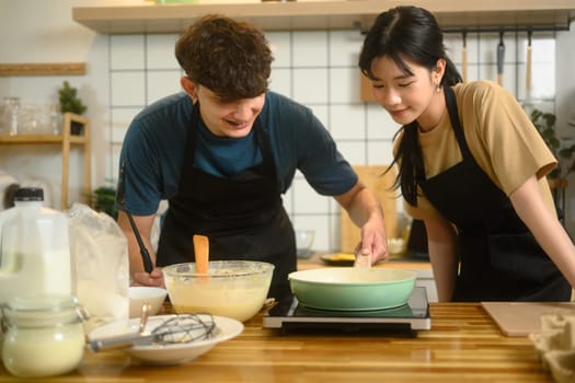 Man and woman wearing aprons and preparing breakfast together in the kitchen.
