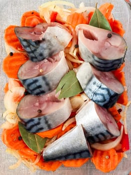 Fresh mackerel pieces laid on a bed of sliced carrots and onions with aromatic spices including bay leaves and peppercorns, prepared for cooking a flavorful dish. Made on smartphone