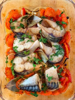 Baked mackerel fillets arranged on a bed of sliced carrots and bell peppers in a clear baking dish. Garnished with fresh herbs and bay leaves for added flavor. Made on smartphone