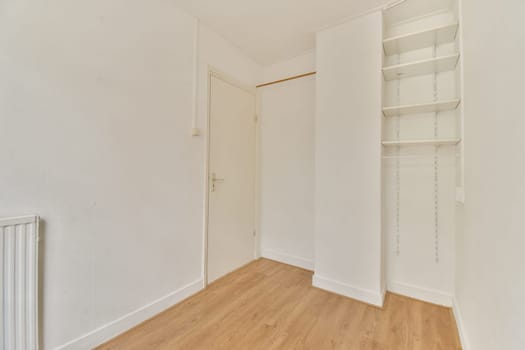 An airy room featuring white walls, a blank doorway, and wooden flooring. The space includes built-in shelves for organized storage.