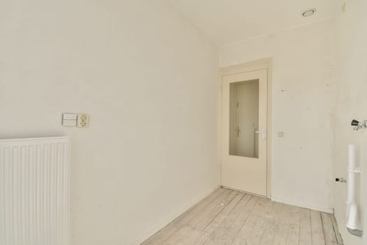 A clean and empty interior space featuring white walls, a light wooden floor, and a simple door. The ambiance conveys a sense of openness and simplicity.