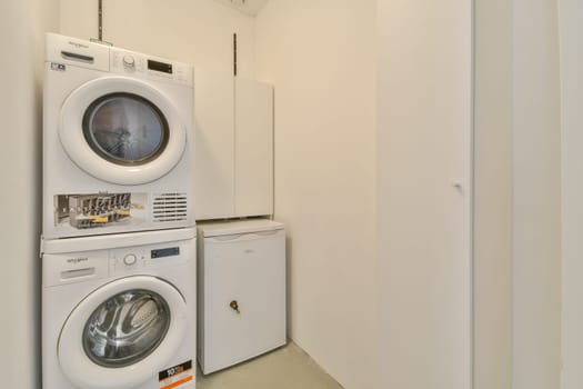 A contemporary laundry room featuring stacked washing machine and dryer, along with a compact refrigerator. The simplicity and cleanliness of the space highlight modern design.