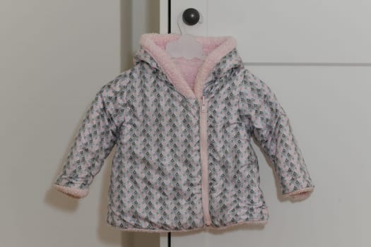 Pink-lilac colored fur jacket for girl hanging on hanger on white background
