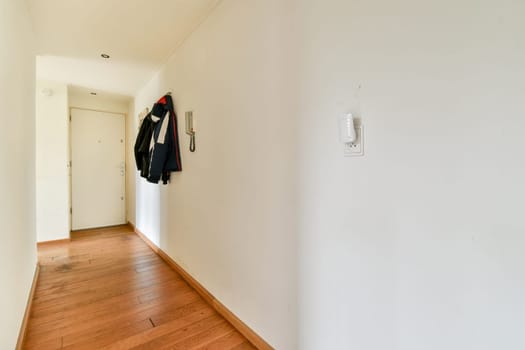 A spacious hallway featuring sleek wooden flooring and a minimalist design, enhanced by natural light and modern decor elements.