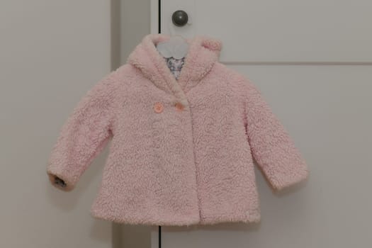 Pink winter artificial fur jacket hanging on a hanger on a white background