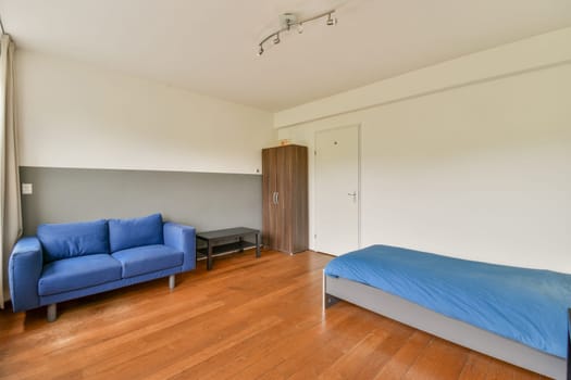 A clean, spacious bedroom featuring a blue sofa, wooden flooring, and minimalist decor elements. The room exudes a calm and relaxing atmosphere.