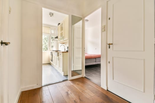 A contemporary hallway connects to a stylish kitchen and a cozy bedroom, featuring sleek designs and wooden flooring that enhance the modern aesthetic.