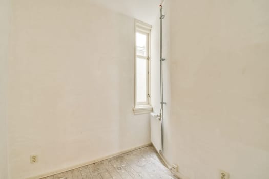 An empty room featuring minimalist white walls and a single window allowing natural light to illuminate the space. The flooring is simple and unobtrusive.