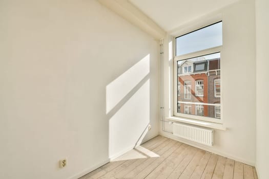 A spacious room featuring a large window that allows natural light to illuminate the area, showcasing its minimalistic design and light-colored flooring.